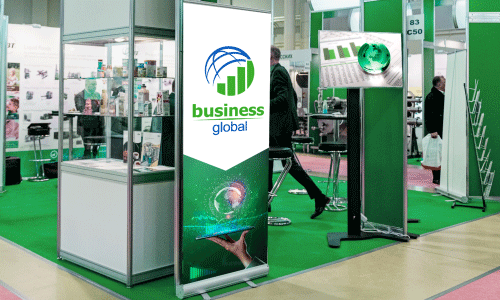 24” x 78” banner retractor lite on a green carpet in a trade show booth. Banner displays a green and white background with a circular logo of half a blue sphere and green bar graph. Large text beneath says Business in green and Global in blue lettering.