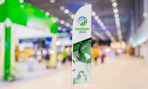 White feather flag with circular logo of half a blue sphere and a green bar graph underneath. The text next to the logo says Business in green text, and Global in blue text. There is a green globe image at the bottom of the flag. The background is a blurry image of a trade show floor.